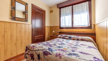 Ein Schlafzimmer mit einem Holzschrank, einem Bett mit Blumendekoration und einem Fenster mit Vorhängen, sowie einem Spiegel an der Wand.
