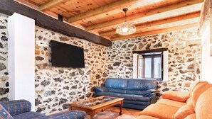 A rustic interior with stone walls, a wooden ceiling, a blue leather sofa, an orange sofa, and a wooden coffee table. - Rural House 'Trasmiera' with Private Terrace, Private Garden and Wi-Fi (Solórzano)