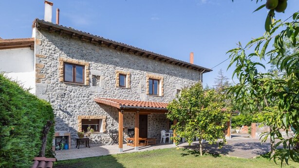A stone house with a tiled roof, a patio with outdoor furniture, and a garden with trees and shrubs. - Rural House 'Trasmiera' with Private Terrace, Private Garden and Wi-Fi (Solórzano)