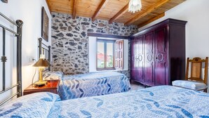 A bedroom with two beds, a stone wall, a wooden ceiling, and a large wardrobe. - Rural House 'Trasmiera' with Private Terrace, Private Garden and Wi-Fi (Solórzano)