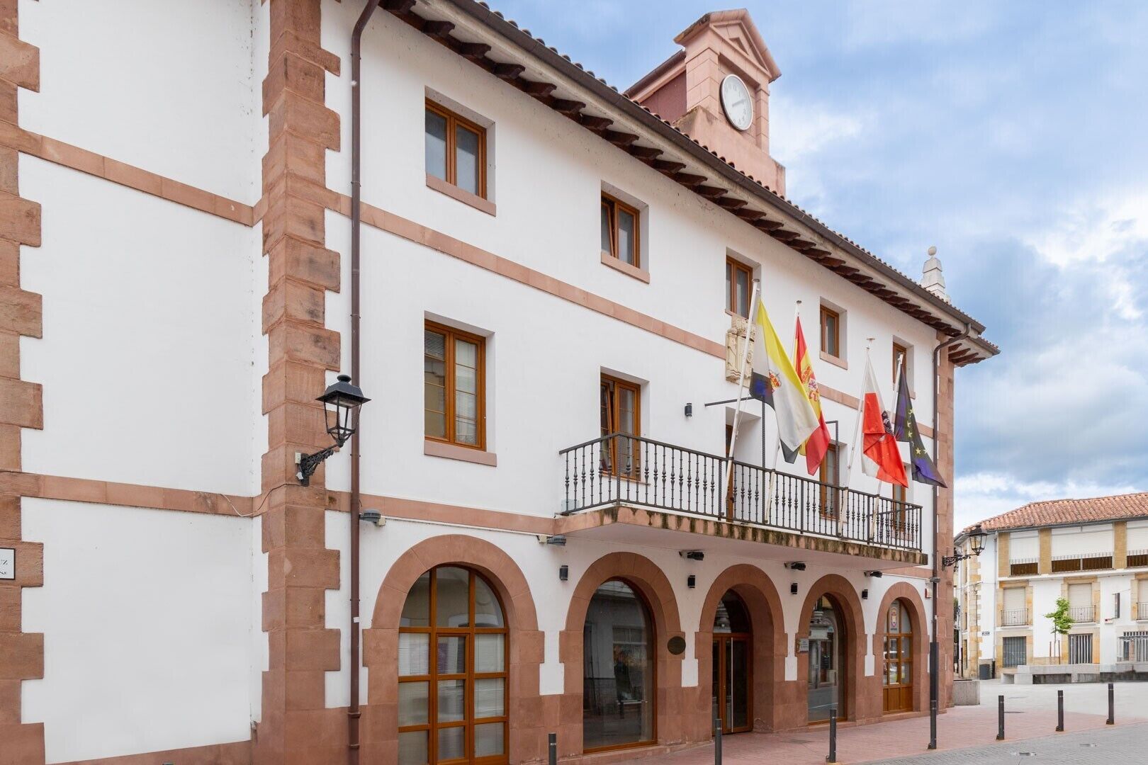 Un edificio con fachada blanca, múltiples ventanas, un balcón con barandillas y varias banderas.