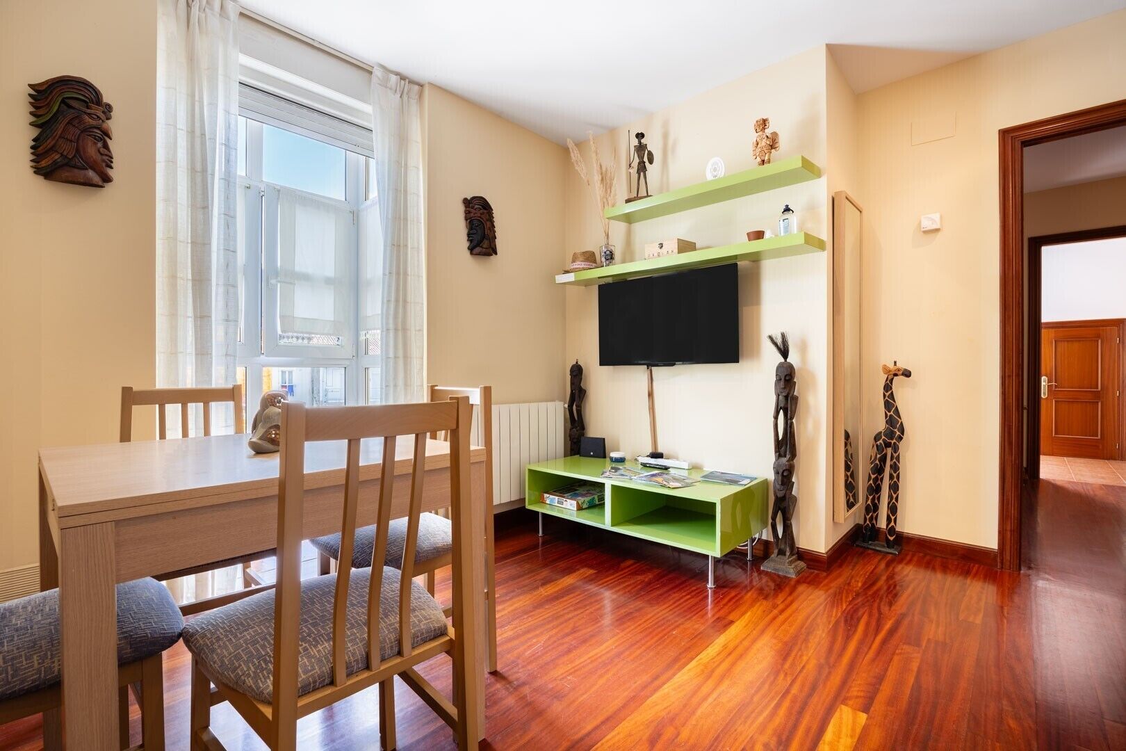 A dining area with a wooden table and chairs, a television on a green stand, and decorative items on the wall.