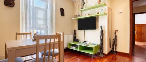 A dining area with a wooden table and chairs, a television on a green stand, and decorative items on the wall.