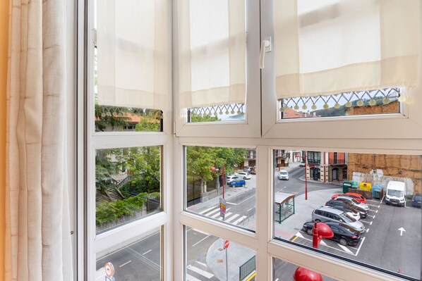 A view from a window with multiple panes, overlooking a street with parked cars and a bus stop.