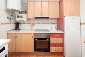 A compact kitchen with wooden cabinets, a built-in oven, a microwave, and a refrigerator.