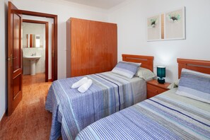 A bedroom with two beds, a wardrobe, a bedside table with a lamp, and a bathroom visible through an open door.