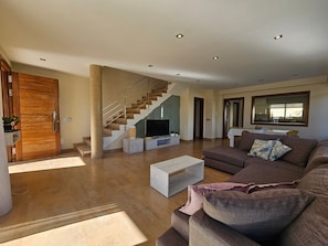 A modern living room with a staircase, a flat-screen TV, and a large mirror.