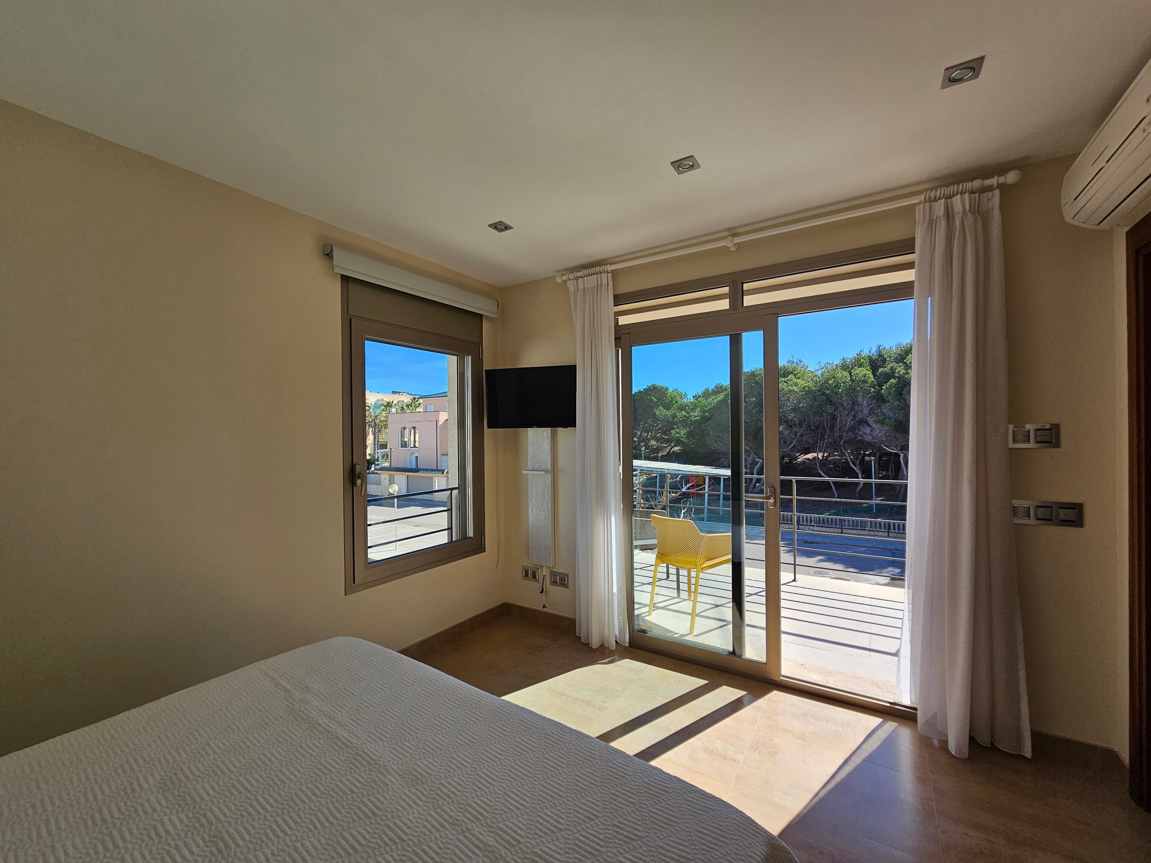 Ein Hotelzimmer mit Bett, Fernseher, einer Glastür zum Balkon und Blick ins Freie.
