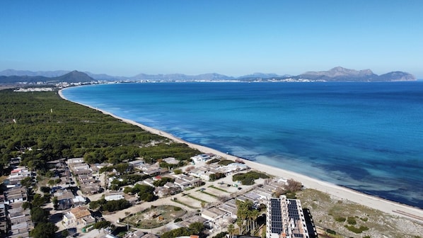 An aerial view of a coastal town with a beach, residential buildings, and a clear blue sea.