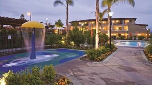 A hotel with a swimming pool, palm trees, and a water feature. - Carlsbad | Short Stay Beach Retreat | Pool + Ocean (Carlsbad)