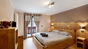 A wooden bed with a headboard, bedside lamps, a wooden nightstand, and a view of a balcony. - Roccia Viva 4061 Maison Gerard Apartment with Mountain View, Garden, and Wi-Fi (Cogne)