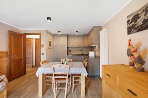 A compact kitchen with wooden cabinets, a dining table with chairs, and a wooden cabinet with drawers.