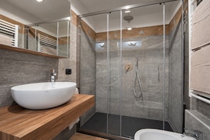 Un bagno moderno con un lavandino bianco di grandi dimensioni, cabina doccia in vetro e mobile contenitore in legno.