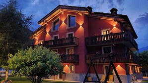 A multi-story building with balconies, a swing set, and a well-maintained lawn. - Roccia Viva 4061 Maison Gerard Apartment with Mountain View, Garden, and Wi-Fi (Cogne)