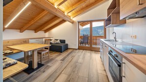 A modern kitchen with wooden beams, a dining area with a bench, and a view through a glass door. - Apartment 'Matscherhof Helena' with Mountain View, Shared Garden and balcony (St. Walburg)