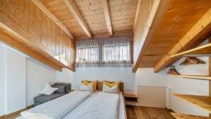 A wooden ceiling, a bed with white bedding, a gray sofa, and a window with curtains. - Apartment 'Matscherhof Helena' with Mountain View, Shared Garden and balcony (St. Walburg)