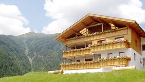 A multi-story chalet with balconies adorned with flowers, set against a mountainous backdrop. - Apartment 'Matscherhof Helena' with Mountain View, Shared Garden and balcony (St. Walburg)