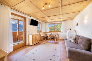 Une pièce avec un plafond en bois, un coin repas comprenant une table et des chaises, un canapé, un téléviseur fixé au mur et une fenêtre donnant sur les montagnes.