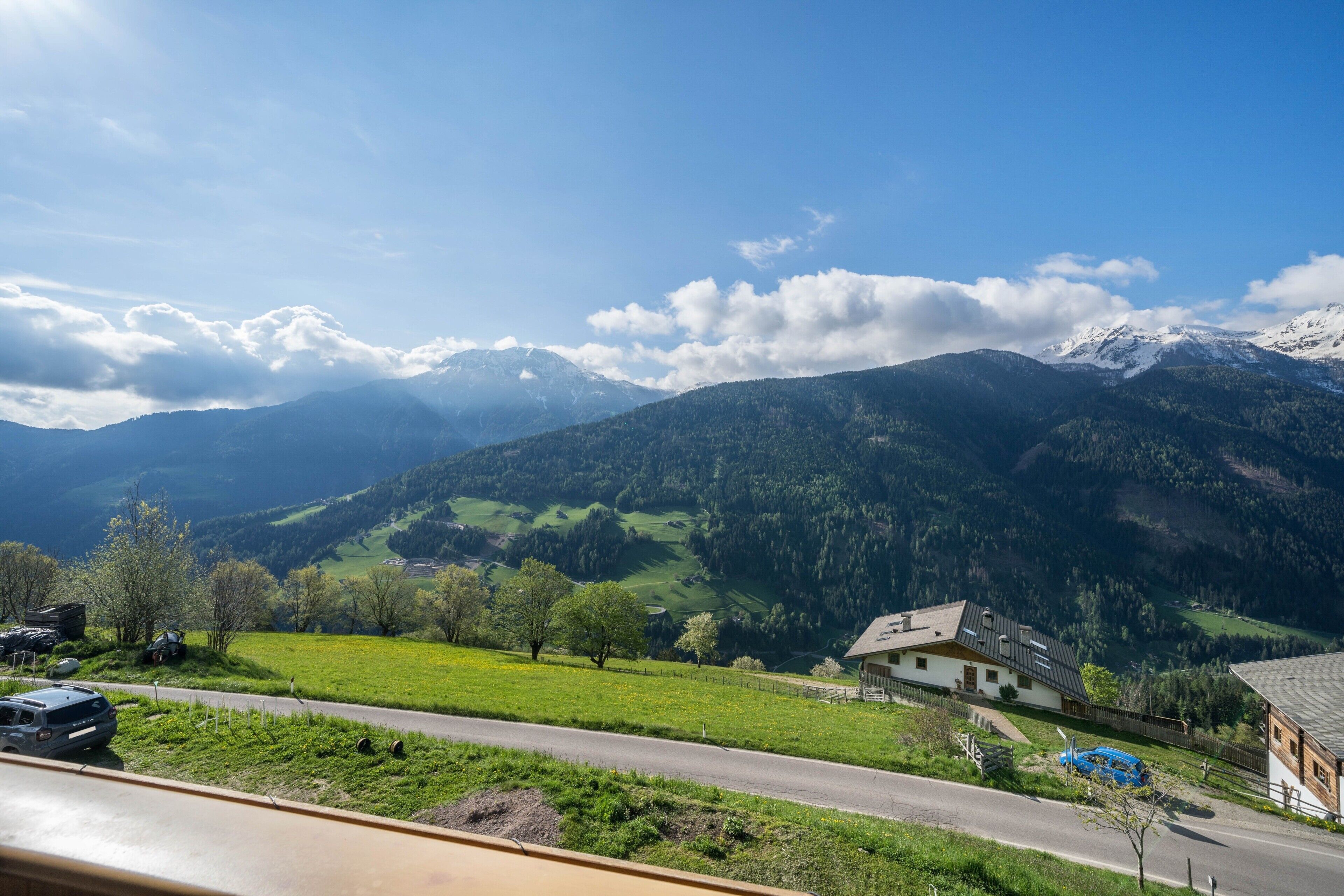 A rural landscape with a road, a house, and mountains in the background.