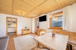 Un intérieur en bois comprenant une table à manger, des chaises, un canapé, un téléviseur et une fenêtre donnant sur la montagne.