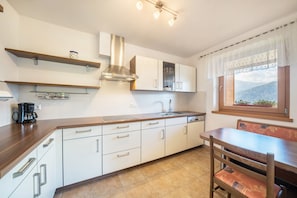 Une cuisine moderne avec des armoires blanches, une hotte de cuisinière en acier inoxydable, une machine à café et un coin repas comprenant une table et des chaises en bois.