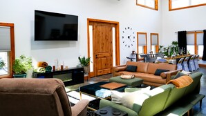 A spacious living room with a large flat-screen TV, a wooden door, and a dining area with chairs and tables. - Black Pearl Lodge @ DeGray. Small event venue or fun family getaway! (Bismarck)