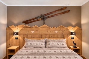 A bedroom with a wooden headboard, two bedside lamps, a bed with patterned bedding, and a ski on the wall.