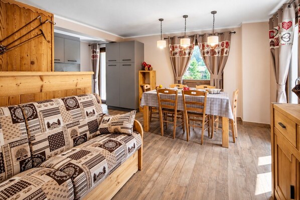 A cozy room with a wooden sofa, a dining table with chairs, and a kitchen area.