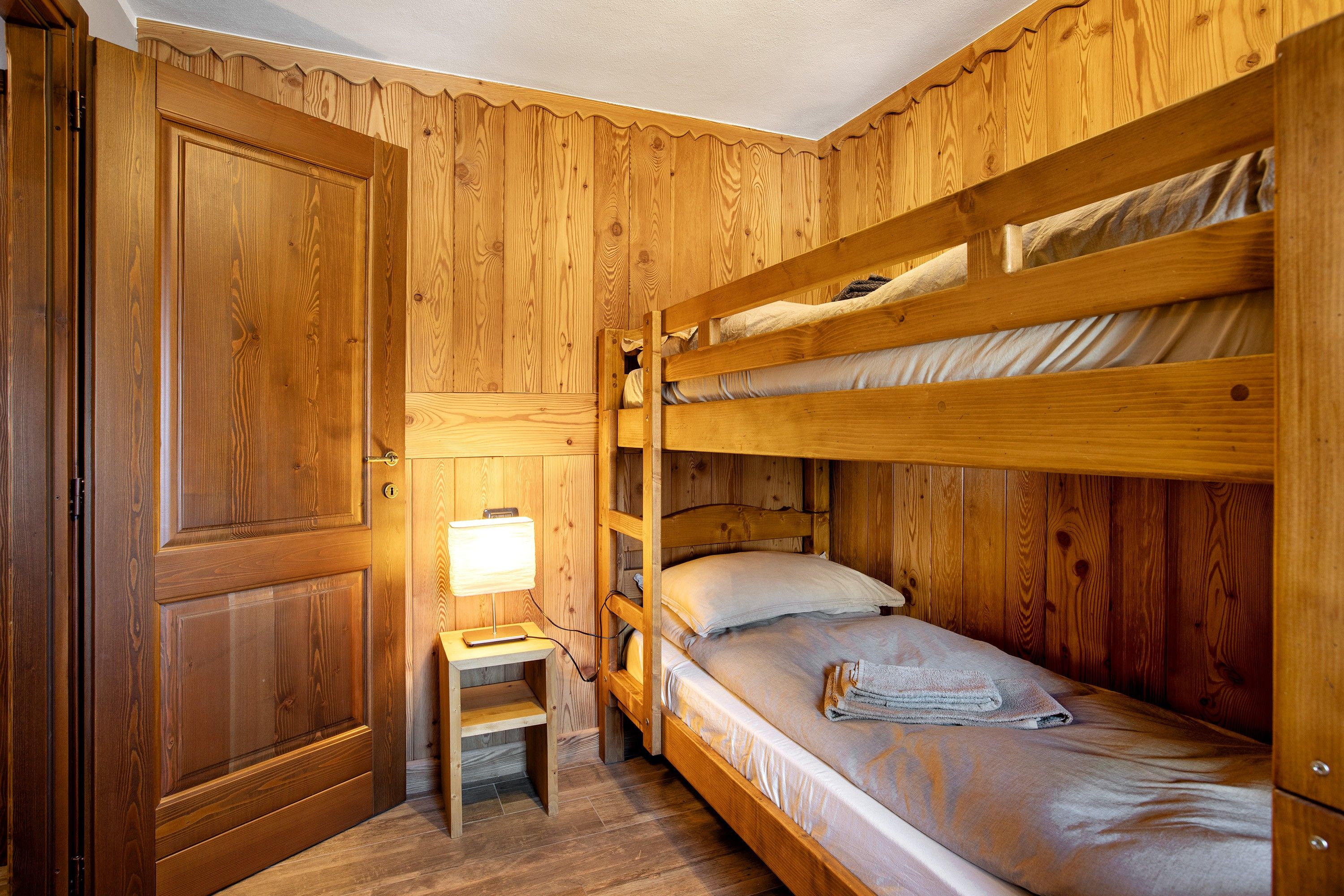 A wooden bunk bed room with a desk and lamp.