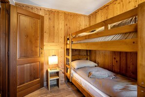 A wooden bunk bed room with a desk and lamp.