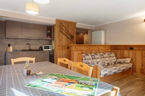 A dining area with a table, chairs, a sofa, wooden walls, a microwave, and cabinets.