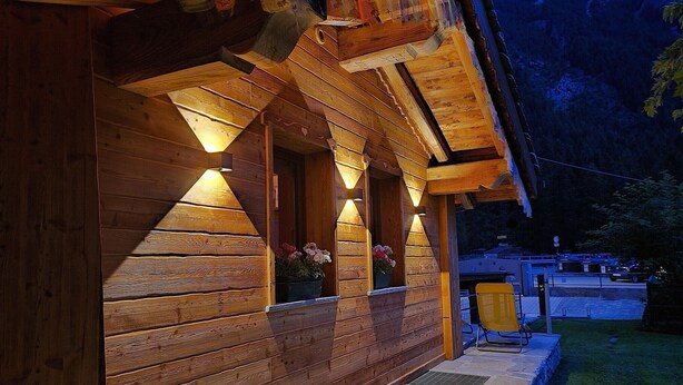 Een houten chalet met een veranda, buitenmeubels en een berg op de achtergrond.