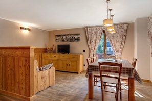 A cozy dining area with a wooden table and chairs, a television on a wooden cabinet, and a painting on the wall.