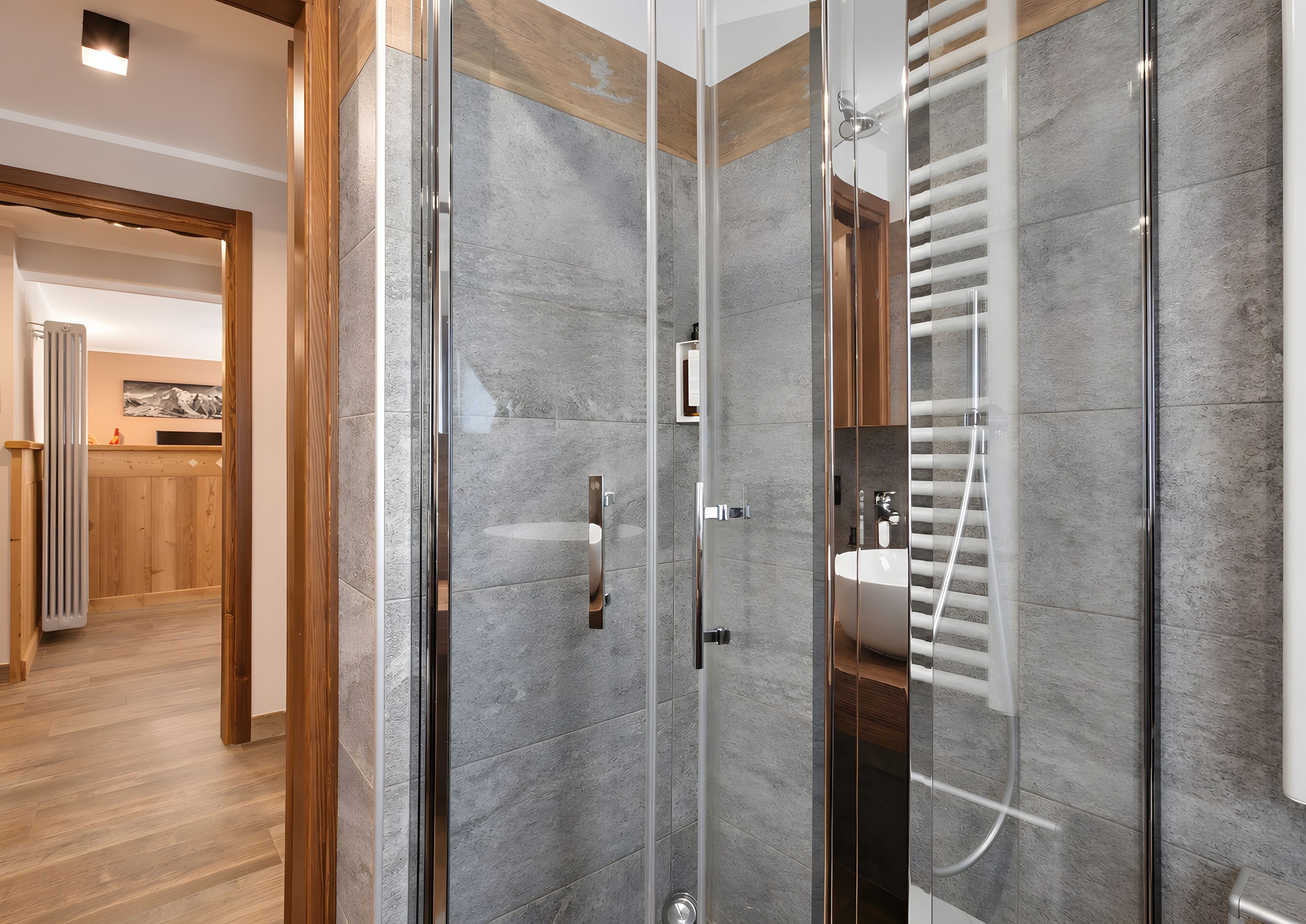 A modern bathroom with a glass shower enclosure, a wooden floor, and a visible sink area.