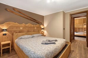 A bedroom with a wooden headboard, a bed with patterned bedding, a nightstand, and a wooden wardrobe.