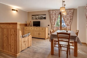 A cozy dining area with a wooden table and chairs, a television on a wooden cabinet, and a painting on the wall.