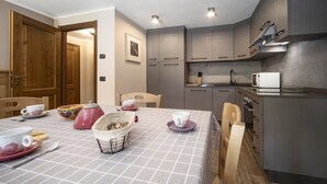A compact kitchen with modern appliances, a dining area with a table set for two, and a wooden door.