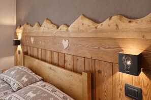 A wooden headboard with a carved mountain design, two heart-shaped cutouts, and a mounted light fixture. - Apartment '4061 Maison Gérard Torre del Gran San Pietro – Svegliarsi tra le Vette' with Balcony, Shared Garden and Wi-Fi (Cogne)