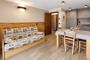 A cozy room with a wooden sofa, a dining table with chairs, and a kitchen area. - Apartment '4061 Maison Gérard Torre del Gran San Pietro – Svegliarsi tra le Vette' with Balcony, Shared Garden and Wi-Fi (Cogne)