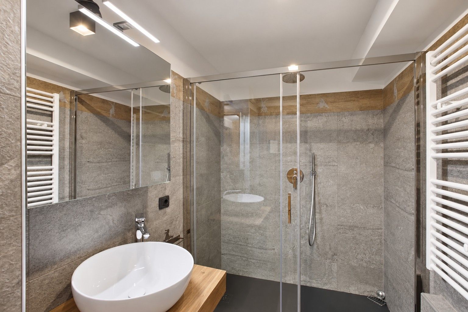 A modern bathroom with a glass-enclosed shower, a white sink, and a wooden vanity.