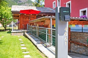 Un buzón con una placa de número, un paraguas rojo y una construcción de madera con un muro de piedra.