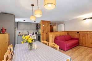 Una habitación acogedora con una mesa de comedor, sillas, un sofá rojo y una zona de cocina al fondo.