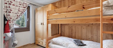 Habitación con literas, paredes de madera, una ventana con cortinas y vistas a árboles.