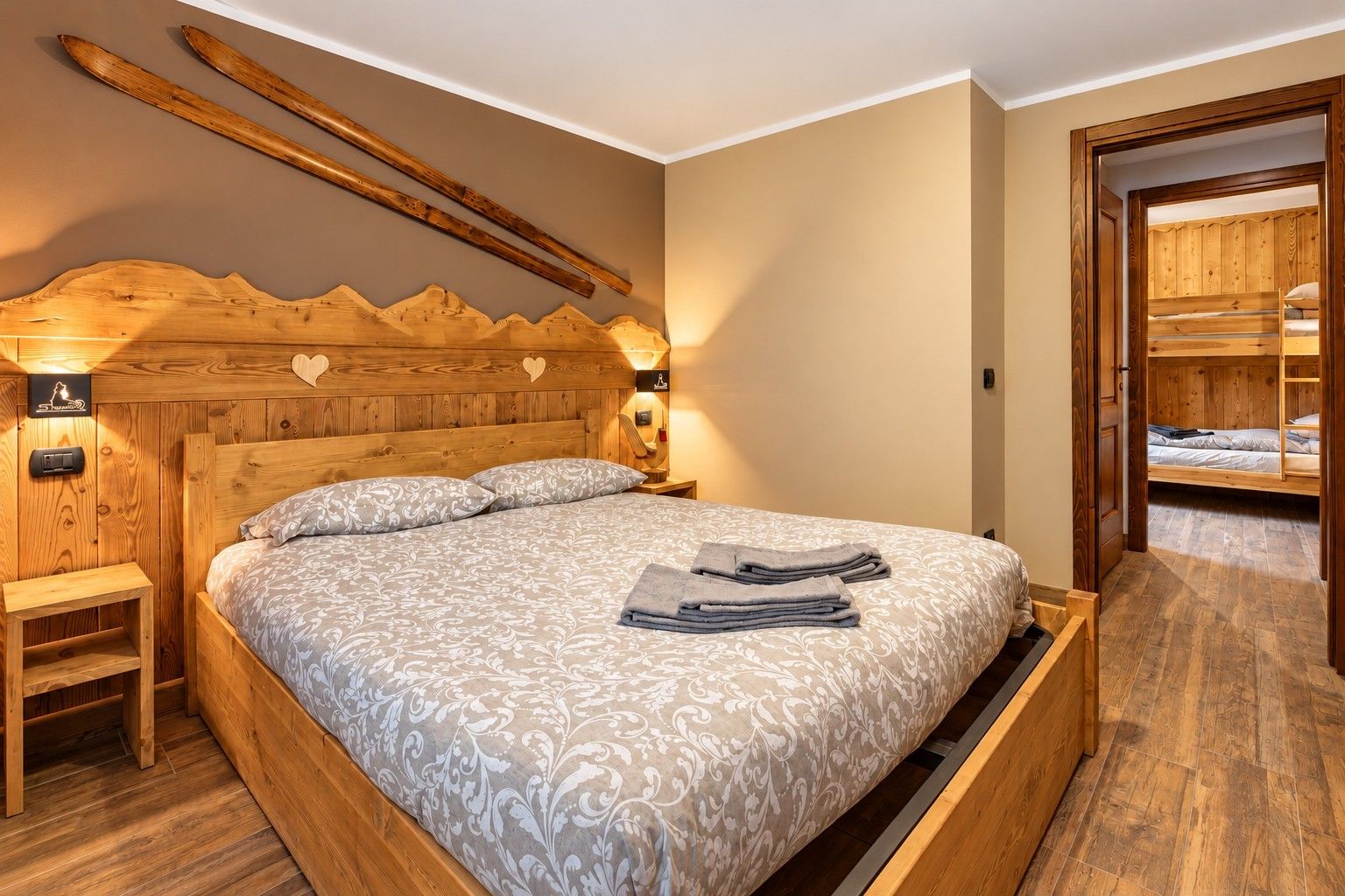 Un letto con struttura in legno, una coperta e cuscini a fantasia, un comodino con una lampada e una parete in legno con porta sci.