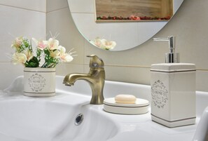 Ein Waschbecken mit einer Messingarmatur, einem Seifenspender und einer Vase mit Blumen.