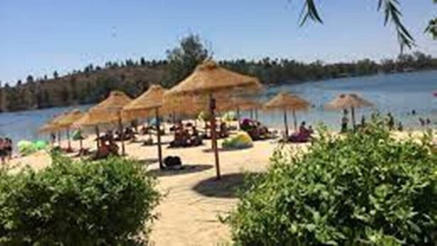 Ein Strand mit reetgedeckten Sonnenschirmen und entspannten Menschen.