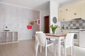 A modern kitchen with white cabinets, a wooden dining table, and white chairs. - Mariva Apartment – Central, Quiet Retreat for a Relaxing Stay (Germignaga)