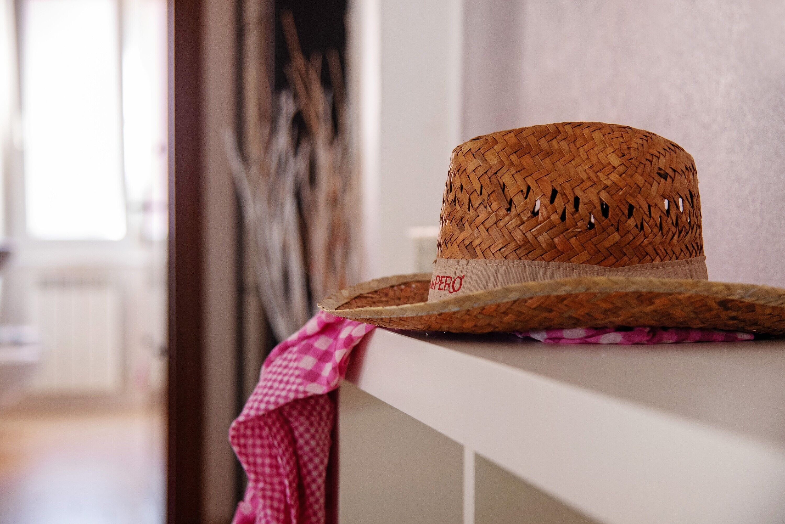 Un sombrero de paja trenzada sobre una superficie blanca con un paño rosa de cuadros.
