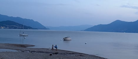 A calm lake with boats, a rocky shore, and mountains in the background.