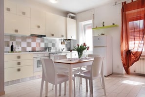 A modern kitchen with white cabinets, a dining table with chairs, and a window with curtains. - Mariva Apartment – Central, Quiet Retreat for a Relaxing Stay (Germignaga)